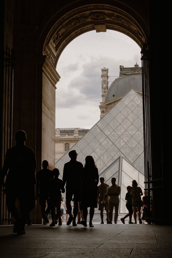 Silhouetted people entering the Louvre with the iconic glass pyramid in view, Paris.