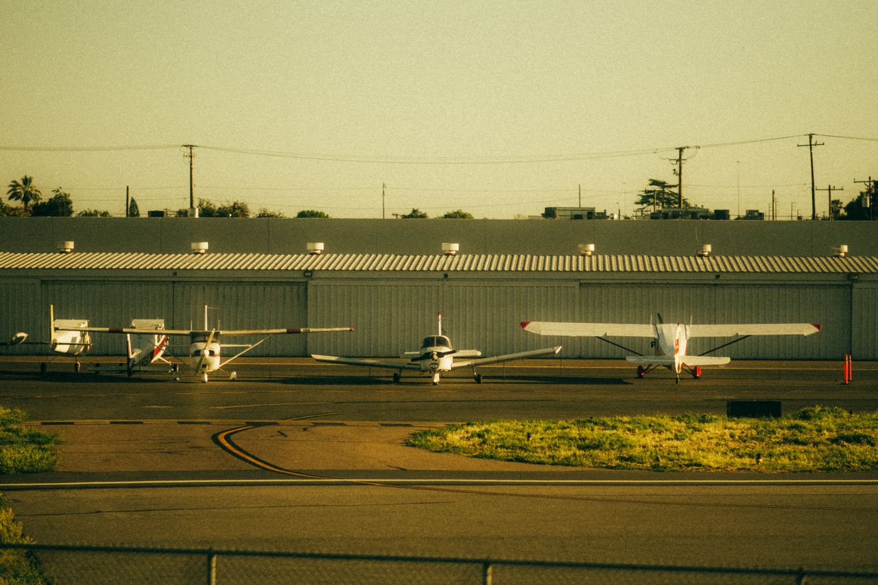 Four private airplanes parked on a sunlit airfield runway, captured at sunset.